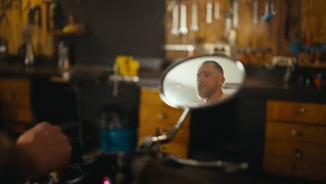 Confident-biker-starts-his-motorcycle-and-is-reflected-in-the-rear-view-mirror-in-his-garage-workshop