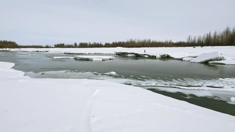 Ein-Auftauender-Fluss-Fließt-Vor-Dem-Hintergrund-Eines-Grauen-Himmels