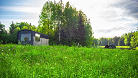 static shot of a wooden cottage and a barrel sauna with dark clouds passing by in timelapse, surrounded by green grasslands and pristine lake at daytime