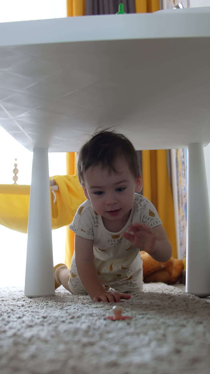 Baby boy crawls under the desk. Happy little kid having fun time at home. Low angle view. Vertical video
