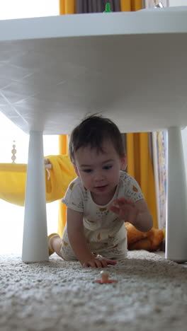 baby boy crawls under the desk. happy little kid having fun time at home. low angle view. vertical video