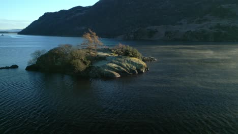 Small-island-in-calm-lake-and-flowing-mist-passing-by-at-sunrise-in-autumn