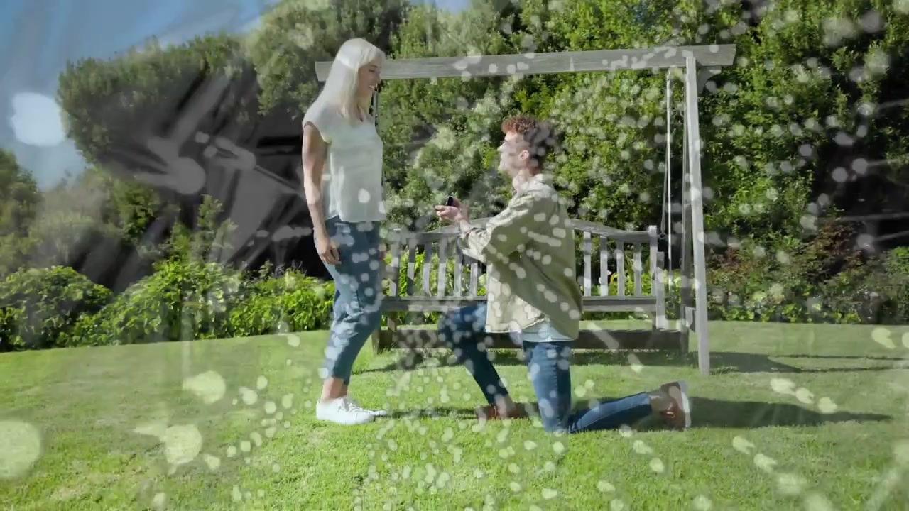 Man kneeling offering engagement ring by swing, woman accepting and embracing under bubbly overlay
