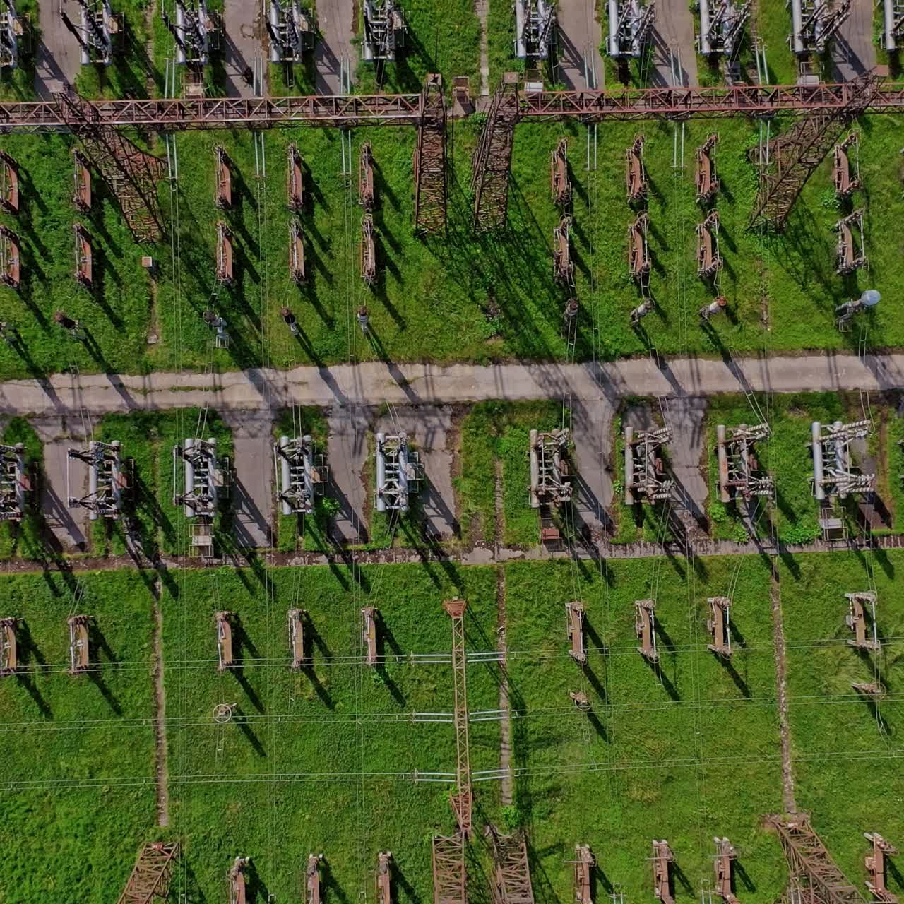 High voltage lines on green field. Power transmission lines. Industrial territory with steel pillars for electricity. Top view. Camera rising up.