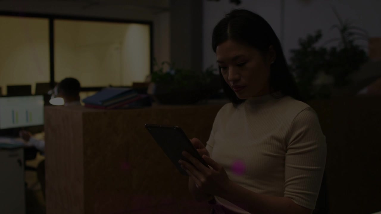Video verticale: Donna in ufficio che tocca un tablet per rivedere i file mentre un bagliore magenta si sposta sul tablet.