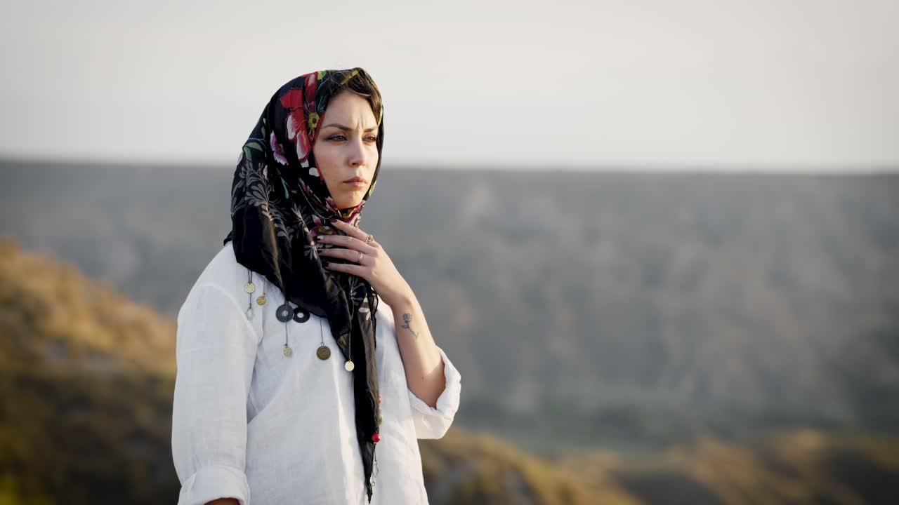 Pensive woman in a traditional headscarf standing in a hilly landscape