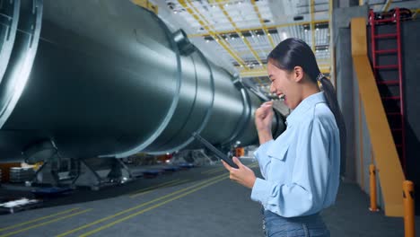 side view of happy asian business woman celebrating using tablet in pipe manufacturing factory