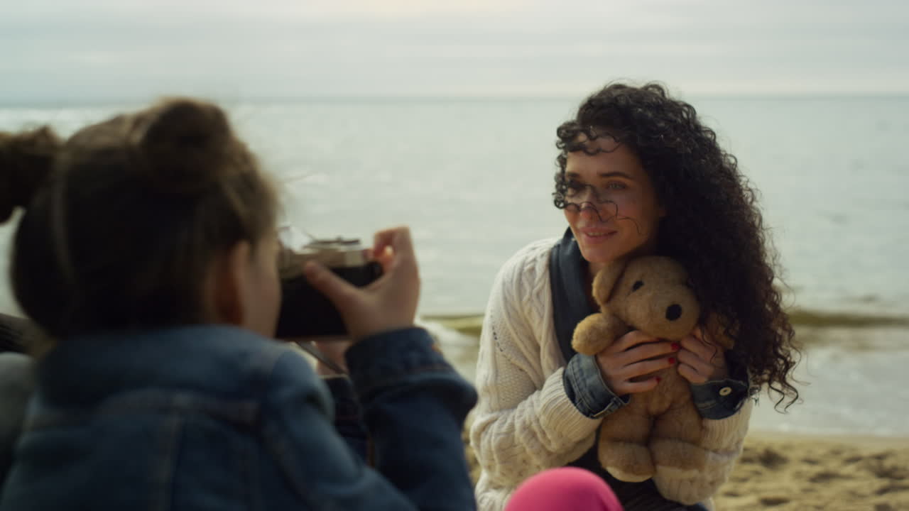 familia jugando con la cámara fotográfica en la playa. padres niño fotografiando oso de peluche