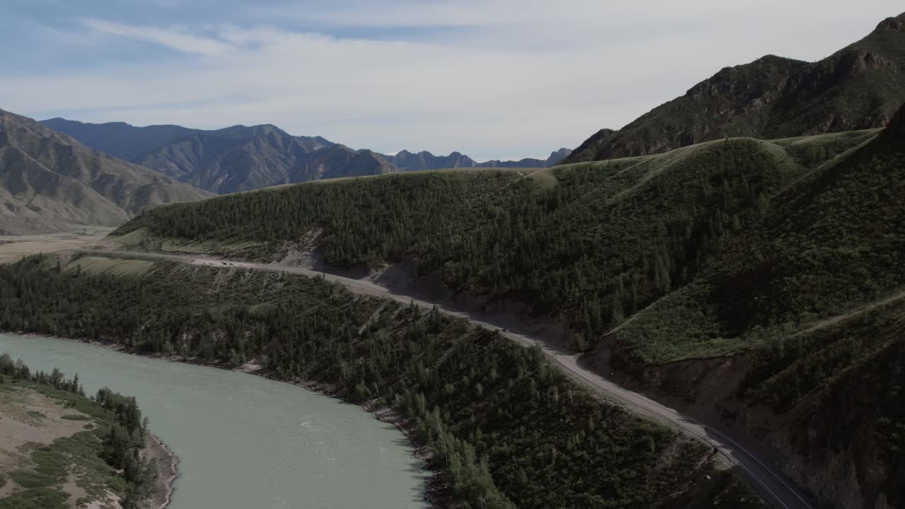 Brede luftoptagelser af den turkise Katun-flod, der snor sig gennem skovklædte bakker langs Chuysky Trakt-motorvejen i Altai-republikken, Rusland, under en skyet himmel