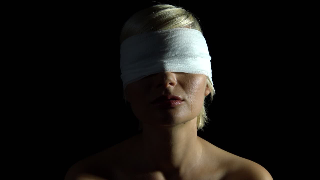 Crying blind folded woman with tears on her chin over black background