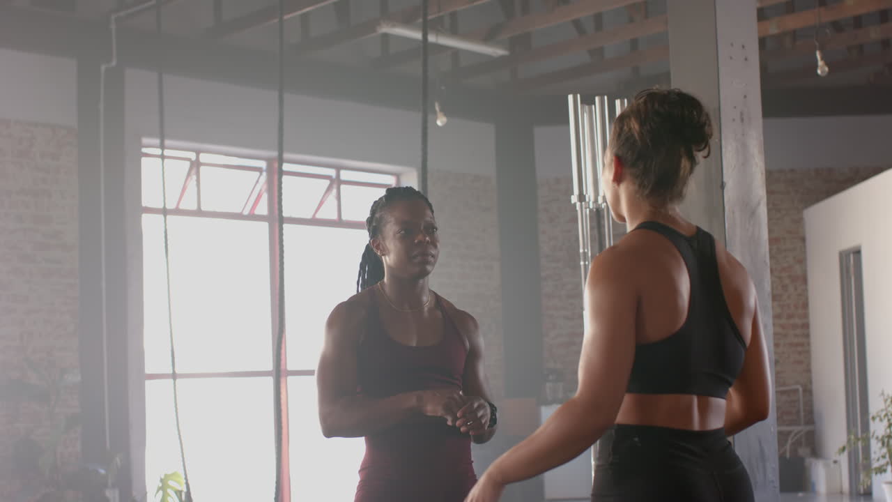 Discussing workout routine, two women in gym wearing athletic clothing