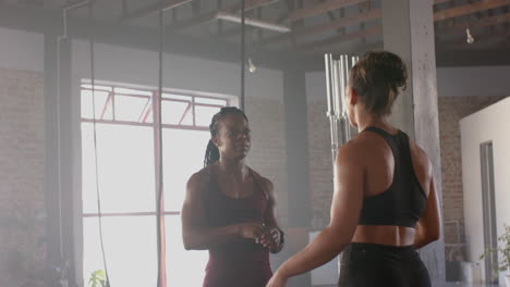 discussing workout routine, two women in gym wearing athletic clothing