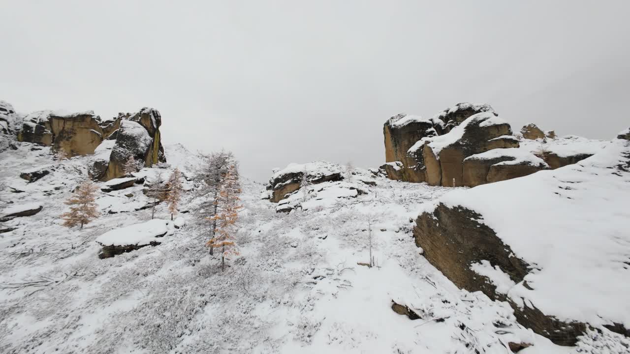 Witness breathtaking winter beauty as a drone captures stunning views of snow-covered cliffs and rocky formations in a serene mountainous region during cold weather.