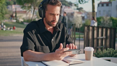 headphones man typing cellphone enjoying music at city park table place close up