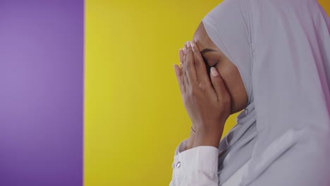 una mujer musulmana africana moderna hace una oración tradicional a dios sobre un fondo colorido.