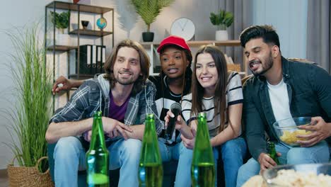 lovely smiling happy carefree young multiethnic friends sitting in front of karaoke setup and singing songs in microphone during cheerful home party