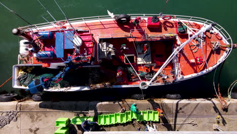 Fishing-vessel-unloads-freshly-caught-fish-into-green-containers,-overhead-drone