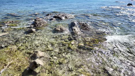 Aguas-Cristalinas-Y-Fondos-Marinos-Rocosos-En-La-Costa-De-Pafos,-Chipre,-Con-Suaves-Olas-Rompiendo-Contra-La-Orilla.