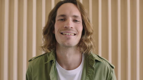 close up portrait of handsome young caucasian man smiling cheerful confident looking at camera relaxed male with long hair wooden backgroud