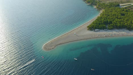 mesmerizing aerial view of beach around crystal clear water of sea, with tourists enjoying paragliding on sunny day