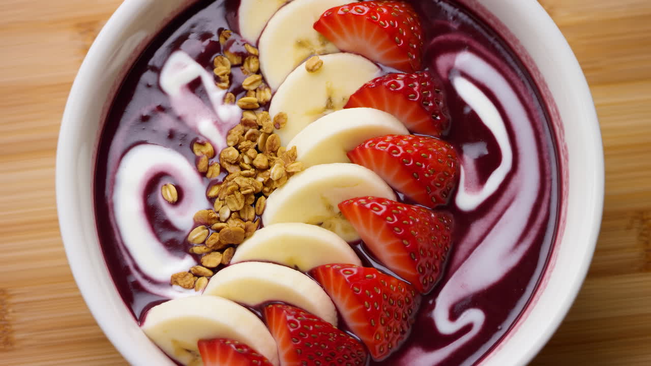 Acai bowl con fette di banana e fragola, base di smoothie viola, spirale di yogurt cremoso e striscia di granola croccante, su sfondo bianco.
