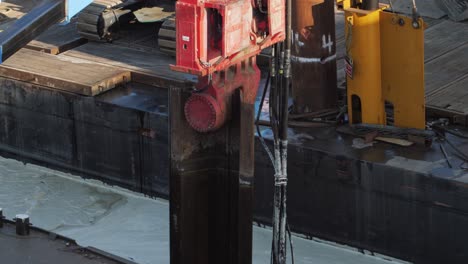 red vibratory hammer pulling a steel sheet pile out of the water during port construction