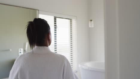Rear-view-of-mixed-race-woman-in-bathroom-taking-bathrobe-off