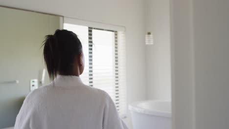 rear view of mixed race woman in bathroom taking bathrobe off