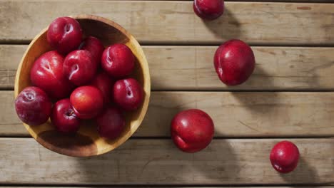 Video-of-fresh-plums-in-bowl-lying-on-wooden-surface