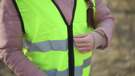 close-up of woman in pink padded jacket fastening zipper on bright yellow reflective safety vest outdoors, preparing for visibility and protection during outdoor