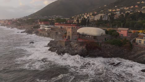 la costa rocosa y los edificios de génova, italia, con las olas chocando contra la costa al anochecer, vista aérea