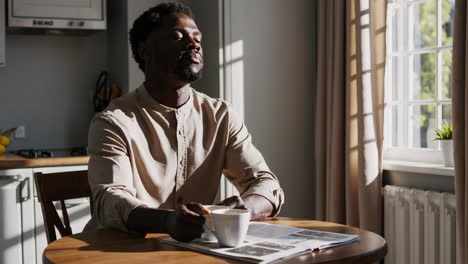 man drinks coffee and reads newspaper in morning kitchen