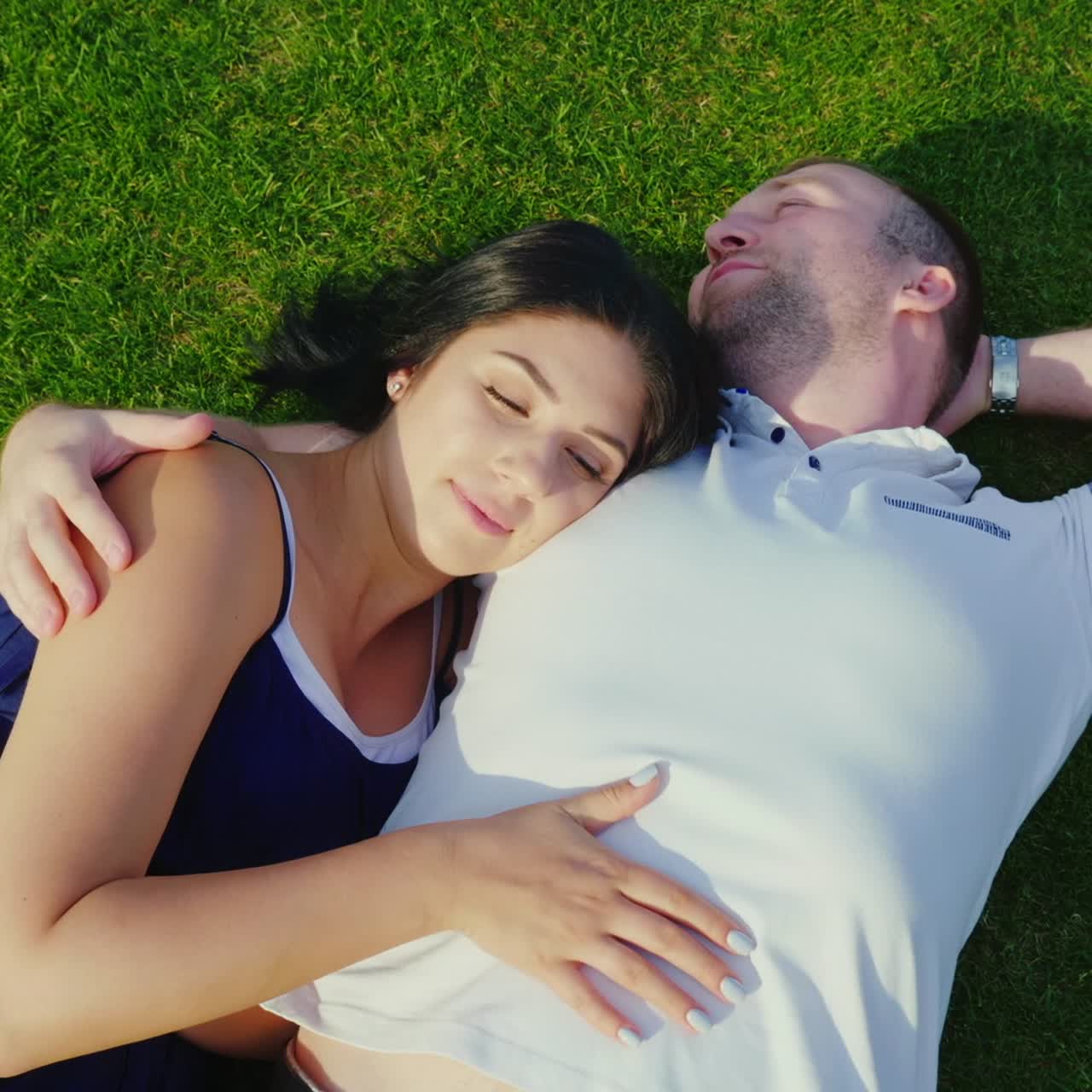 녹색 잔디에 누워 임신한 아내와 남편의 상위 뷰