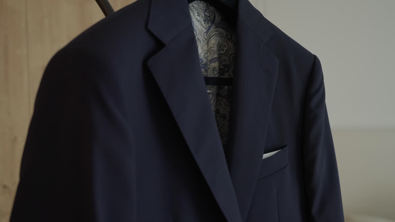 Vista ravvicinata di un'elegante giacca da completo blu appesa a una gruccia, con fazzoletto da taschino bianco e fodera a fantasia all'interno