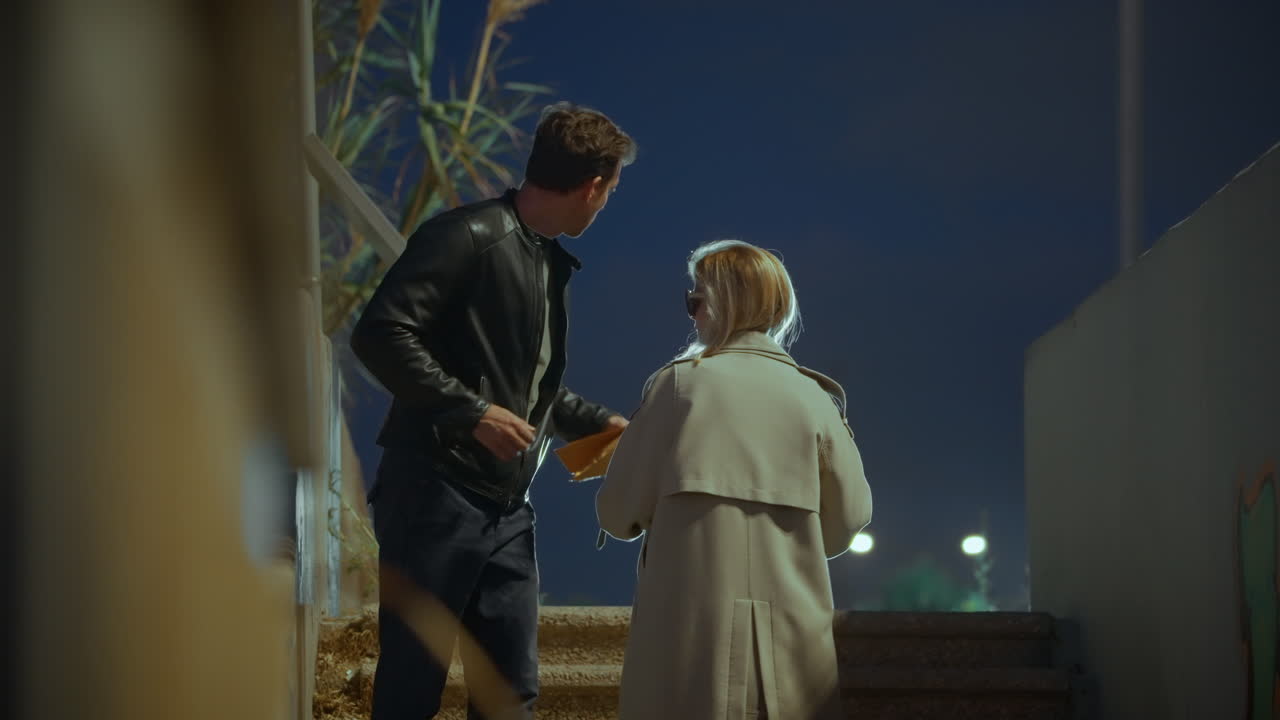 Man meeting with female agent giving him envelope in secret meetup in street at night. Conspiracy or bribe money. Dark corrupted deal. Information exchange. Spy or mole trading secrets or cash payment