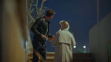 man meeting with female agent giving him envelope in secret meetup in street at night. conspiracy or bribe money. dark corrupted deal. information exchange. spy or mole trading secrets or cash payment