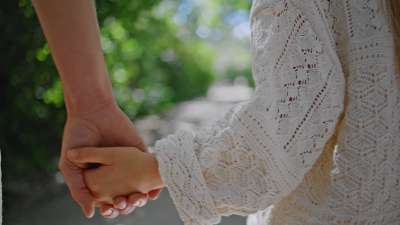 Mom child holding hands strolling summer greenery closeup. Woman girl walking