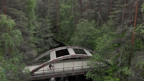 drone flight over a bridge in the middle of a dense forest and a person traveling by bicycle