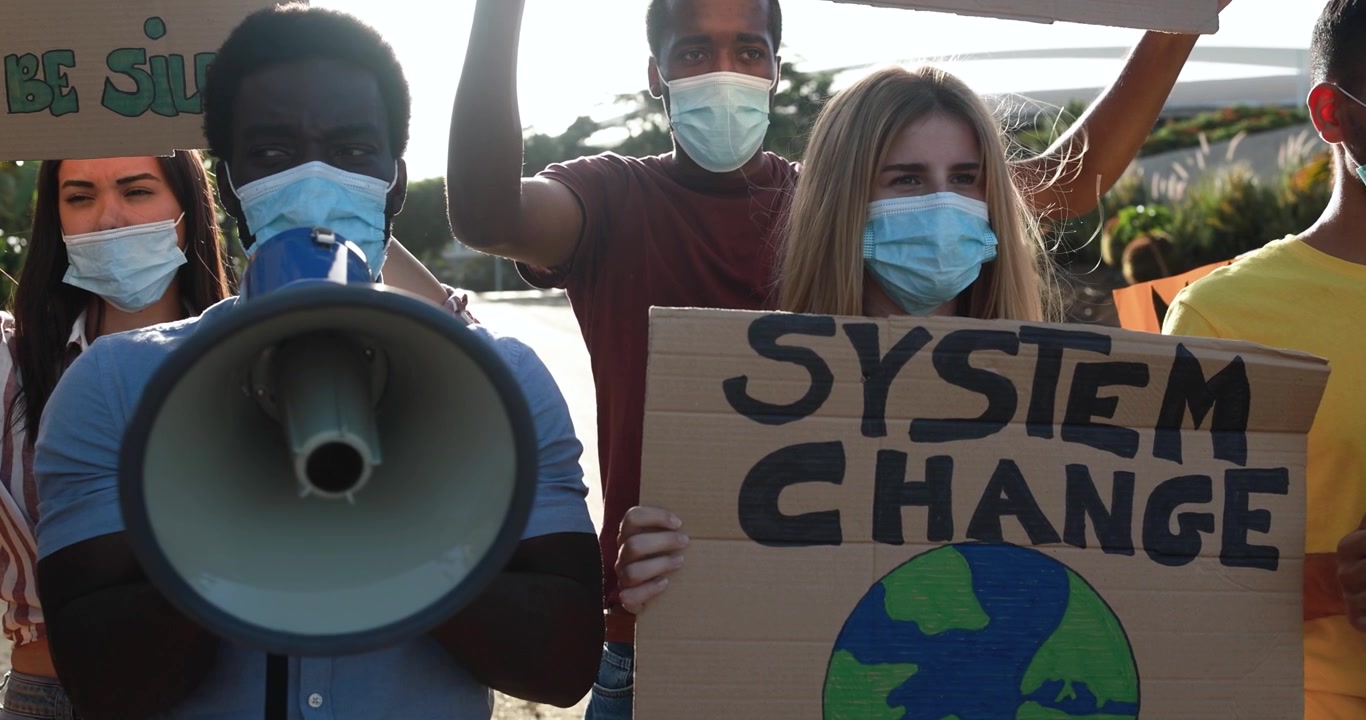 Giovani diversi che protestano per il cambiamento del sistema con megafono e cartelli