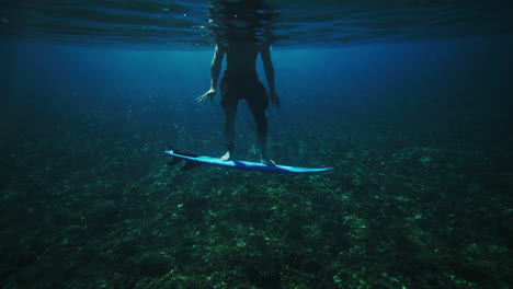 Sideview-of-surfer-standing-on-shortboard-balancing-waving-hands-around-in-water,-underwater