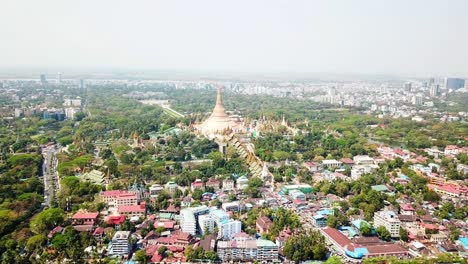 un dron captura la pagoda shwedagon, una magnífica estupa dorada, rodeada de exuberante vegetación y desarrollo urbano en yangon rangoon, myanmar, mostrando la mezcla de vida religiosa y moderna de la ciudad.