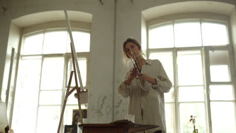 Talented-woman-holding-brushes-indoors.-Creative-painter-standing-near-easel.