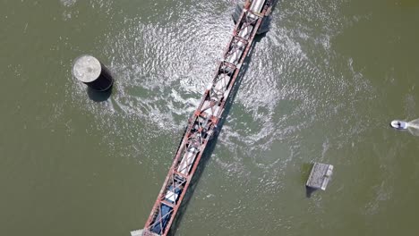 cargo or transit passenger train commuting in bridge over river as a boat travels near by. aerial birds eye orbiting shot