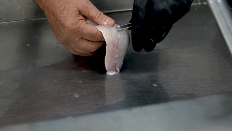 a skilled chef demonstrates precise fish filleting techniques in a bustling local market. the chef carefully handles fresh fish, showcasing professional methods that ensure quality