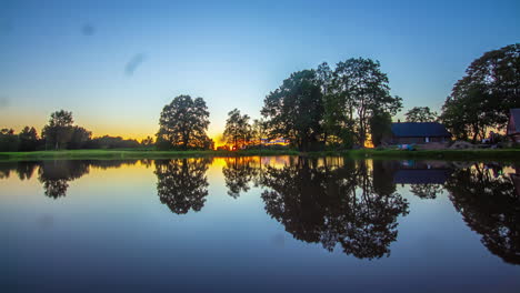 timelapse shot of beautiful sunset in the background over wooden cottages beside a lake during evening time