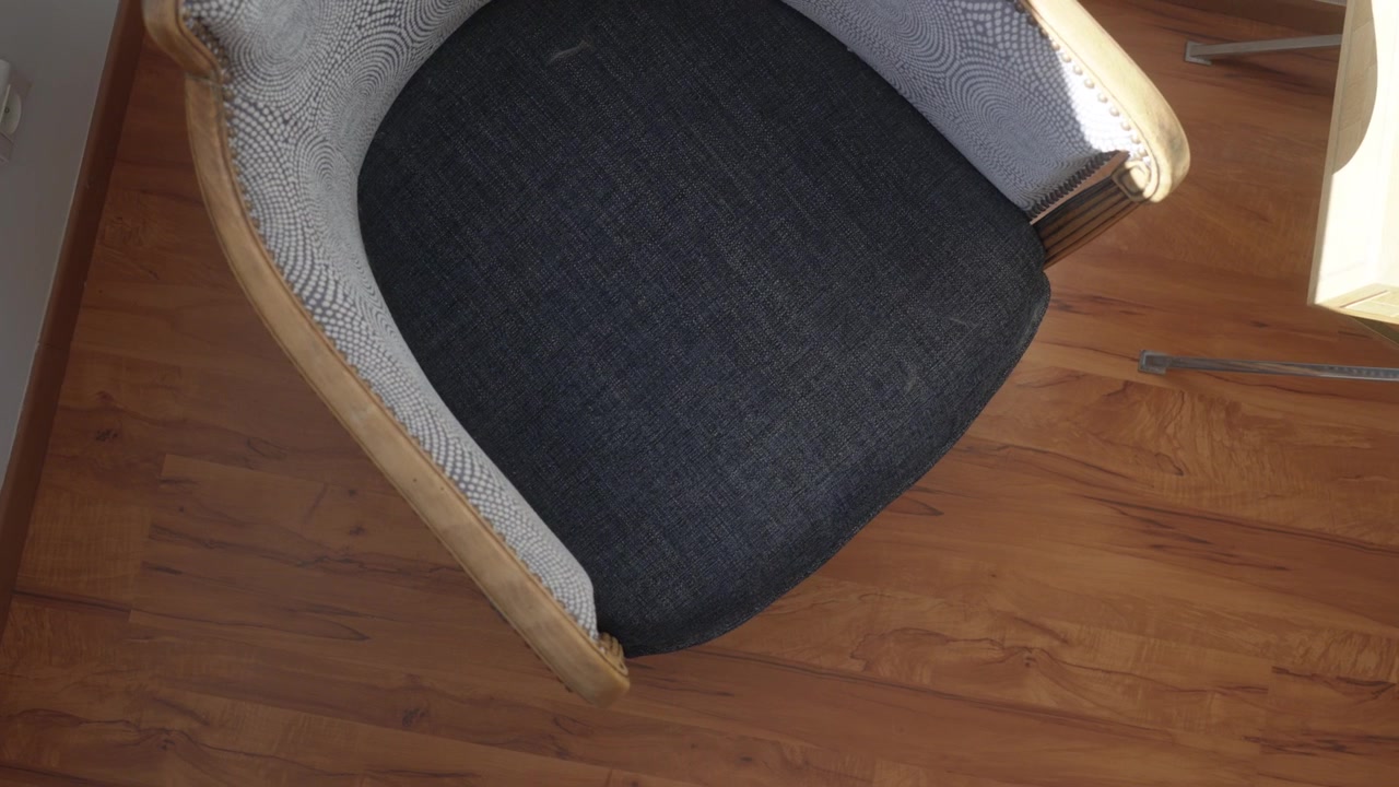 rotasting push in shotof a dark gray upholstered chair with wooden frame on warm hardwood floor, cozy interior, soft indoor light.