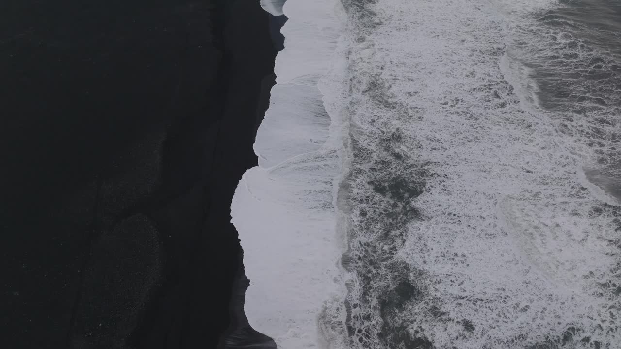 Aerial top view of ocean waves crashing on Iceland S&oacute;lheimasandur black sand beach, on a moody evening