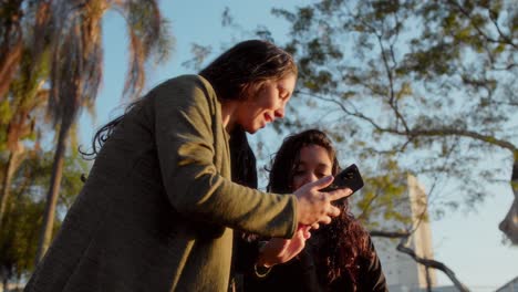 two women interacting with a smartphone in a park