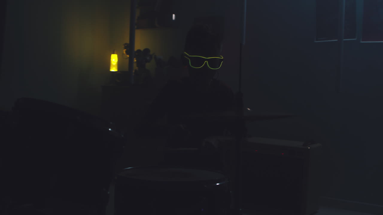 Teenager Playing Drums during Home Concert Zoom out View of Teen Musician in Sunglasses Playing Drums under Blue Neon Illumination and Pretending to be Rock Star during Home Concert in Bedroom