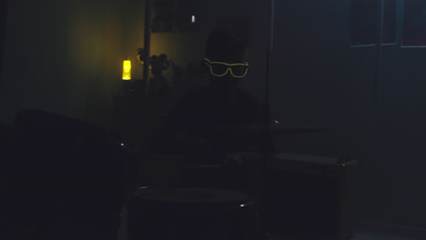 teenager playing drums during home concert zoom out view of teen musician in sunglasses playing drums under blue neon illumination and pretending to be rock star during home concert in bedroom